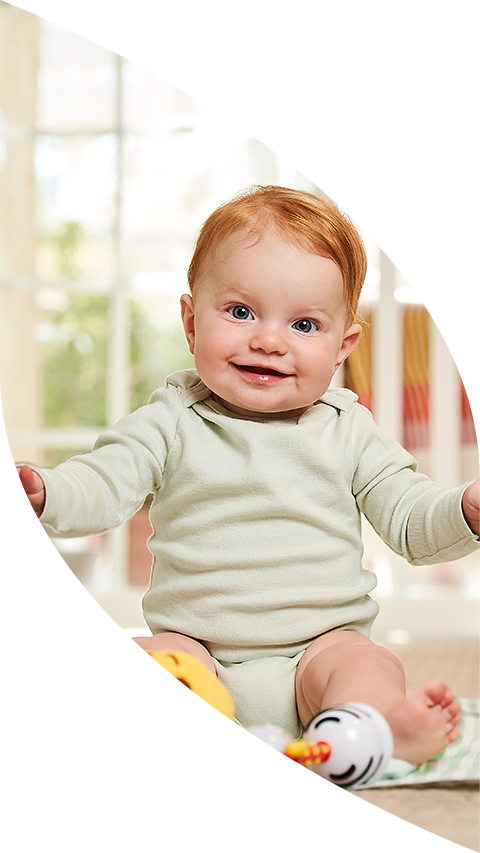 A baby sitting on the ground smiling.