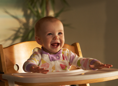 A baby in a highchair, happy, and excited for food.