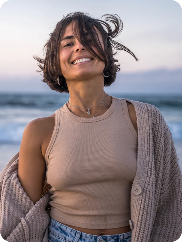 A woman at the beach smiling at the camera.